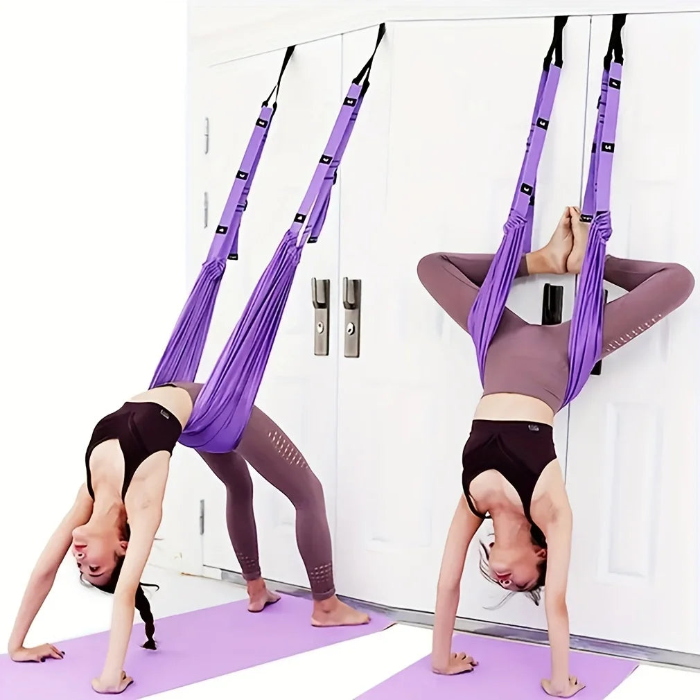 Two people practicing aerial yoga using purple hammocks in a room with a white door.